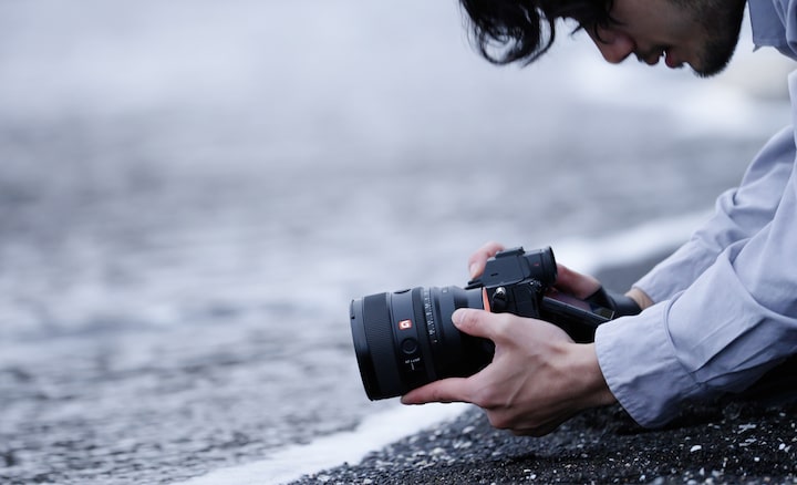 Se ve a un fotógrafo arrodillado al borde del agua capturando fotos en un ángulo que sugiere que podría estar sumergido en el mar.