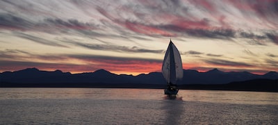 Imagen que muestra un velero en un lago frente a una puesta de sol con un cielo con nubes y colinas oscuras