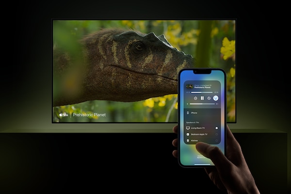 Televisor instalado en la pared con una captura de pantalla de una cabeza de dinosaurio y una mano que sostiene un smartphone